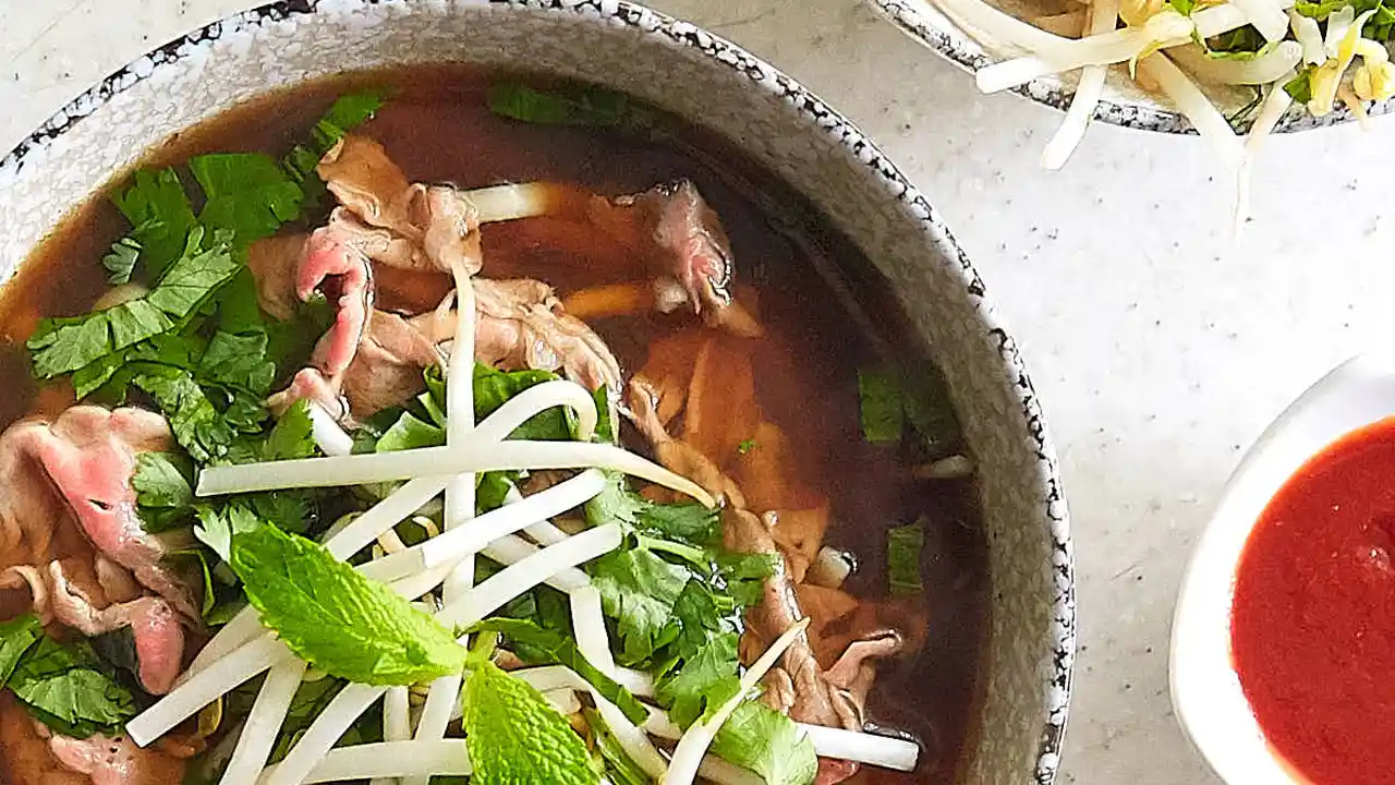 blue bowl of black bean beef tortilla soup on a board with cilantro and shredded cheese in background
